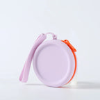 Uma bolsa redonda lilás com zíper laranja e alça de pulso da mesma cor da bolsa.