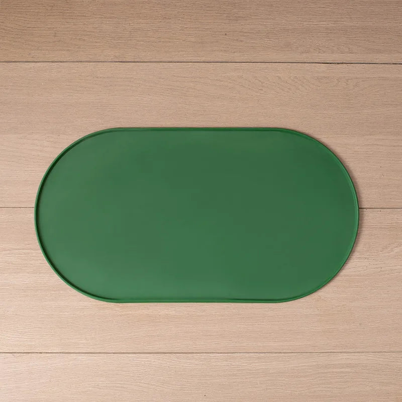 Tapete oval verde para alimentação de pets, com borda elevada, estendido sobre um piso de madeira.