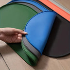Uma mão levantando a borda de um tapete oval azul sobre uma pilha de várias cores. A opção selecionada fornece um tapete.