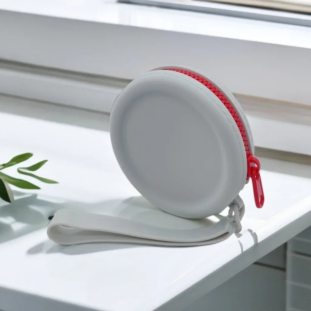 Uma bolsa redonda cinza com zíper vermelho e alça cinza no parapeito de uma janela.