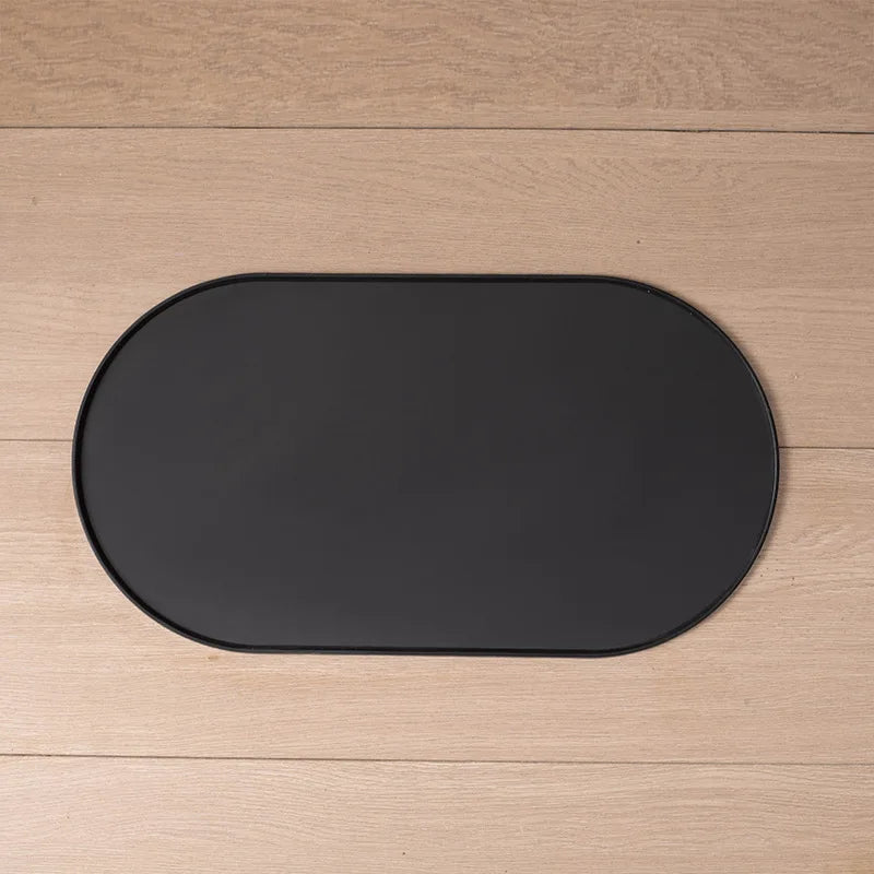 Um tapete oval preto com bordas elevadas, estendido sobre um piso de madeira.