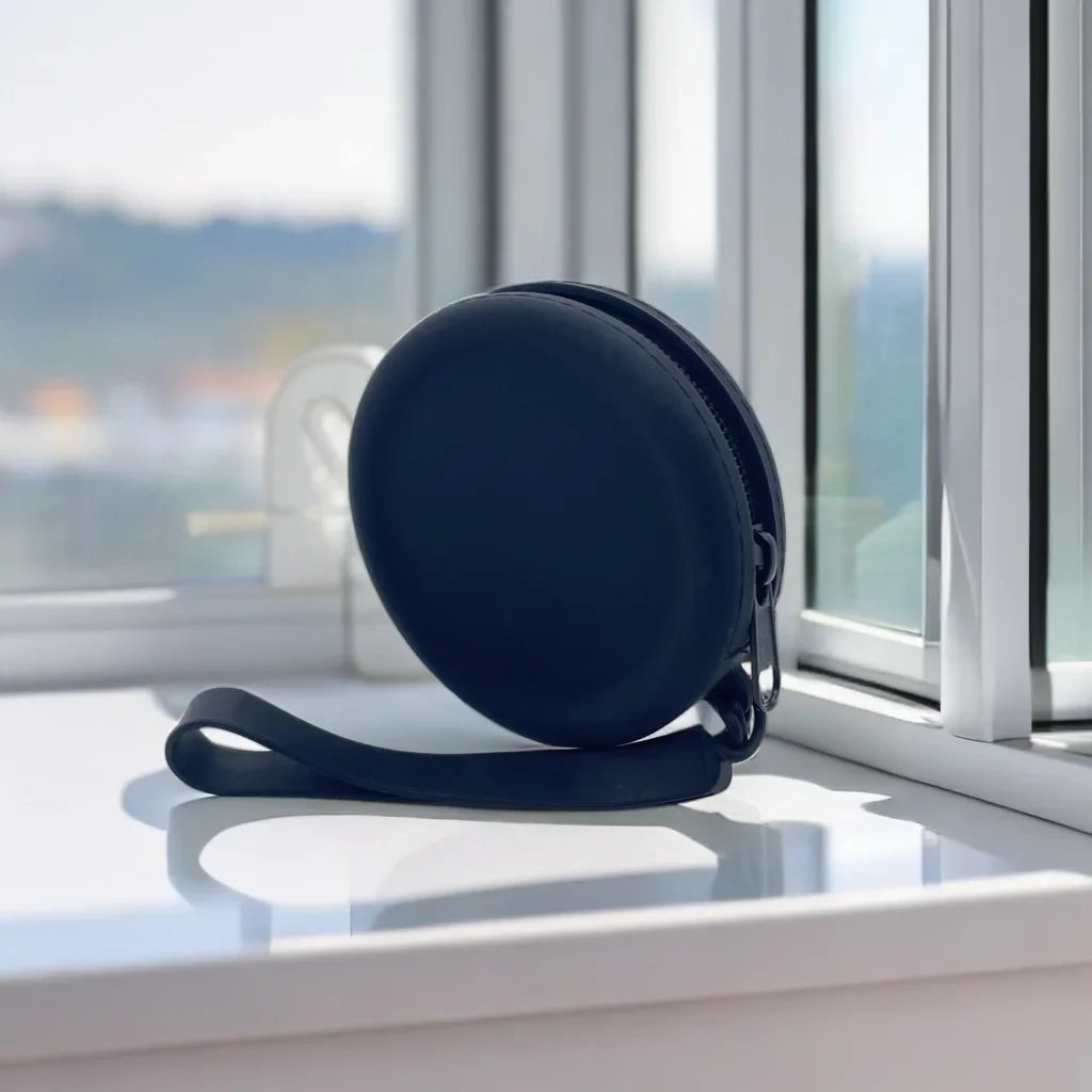 Uma bolsa redonda escura com zíper e alça escuros, junto a uma janela.